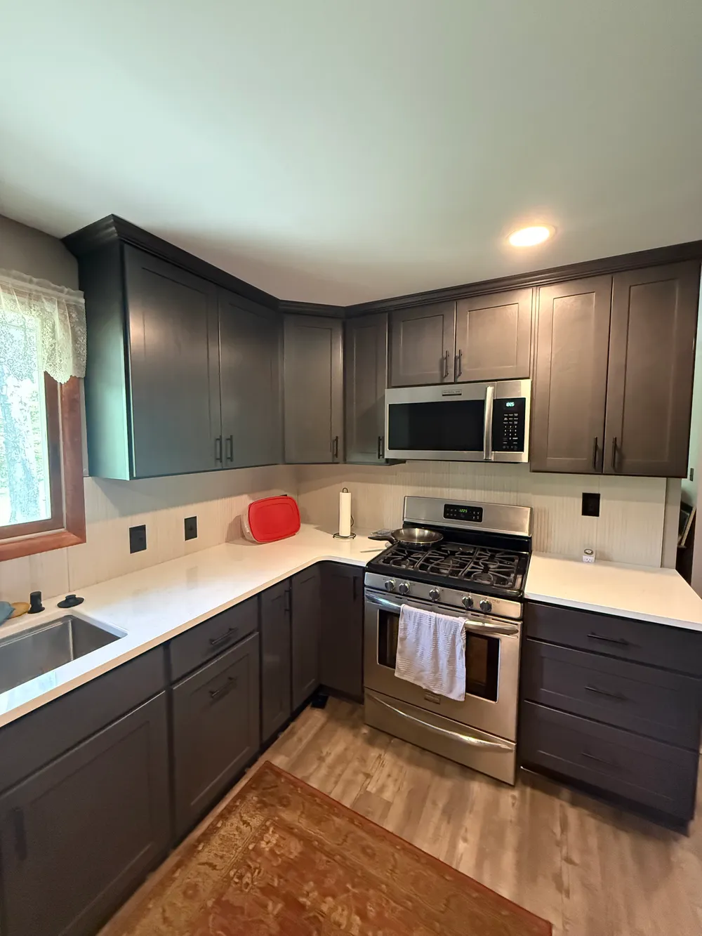 Charcoal kitchen cabinets and crown molding around a stainless steel range, with light counters and backsplash.