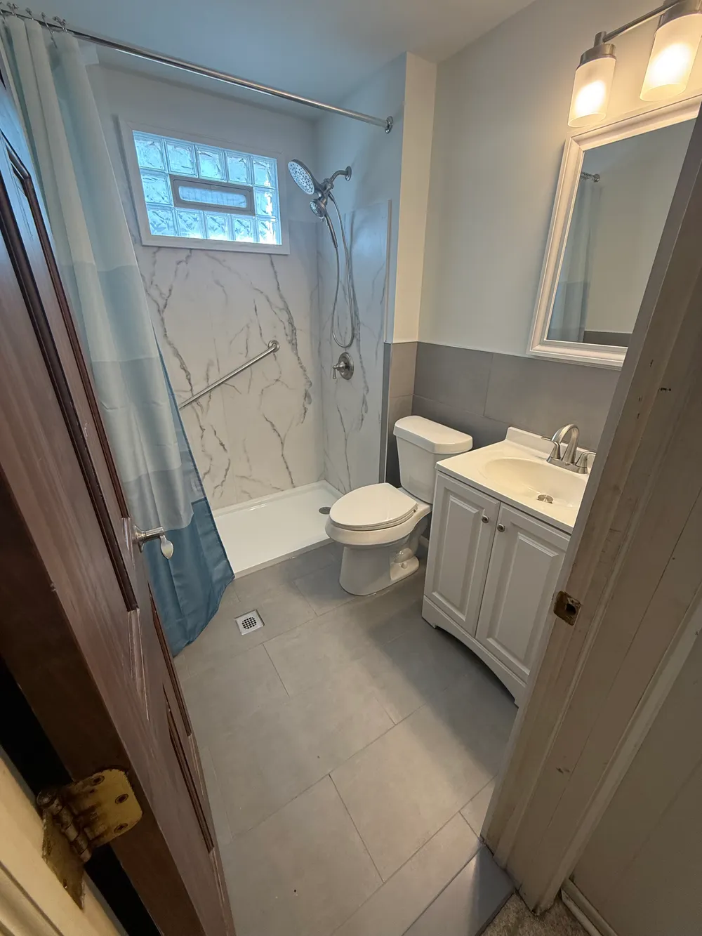 Bathroom with a white vanity, gray floor tiles, and a walk-in shower with a veined wall finish and grab bar.