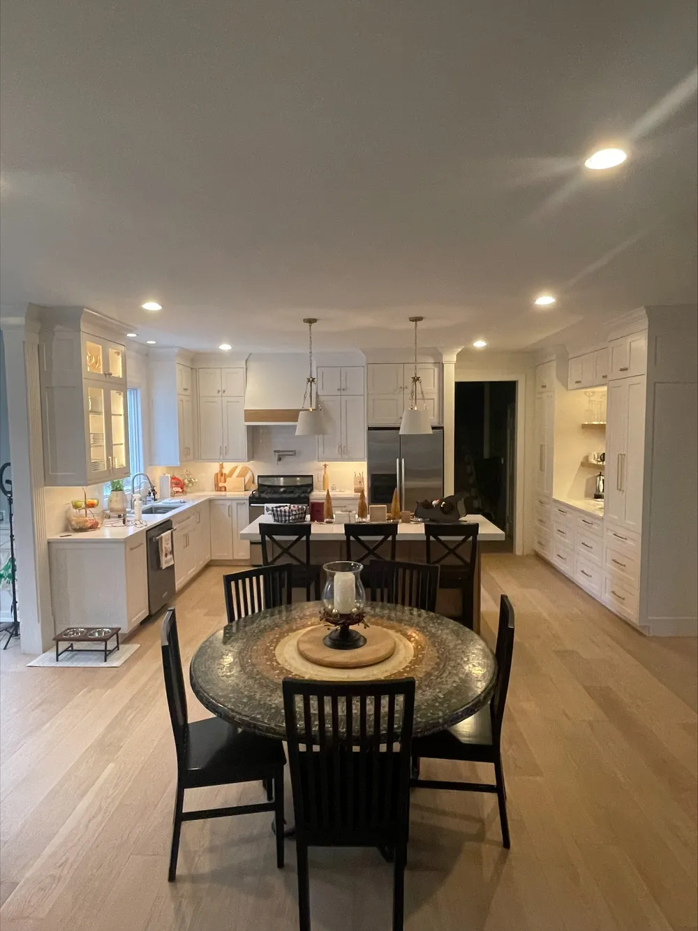 White kitchen cabinetry, an island with pendant lighting, and a dining area.